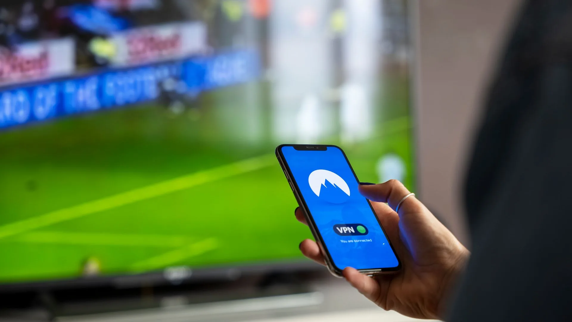 Person strømmer sport på TV med VPN-app på smarttelefonen